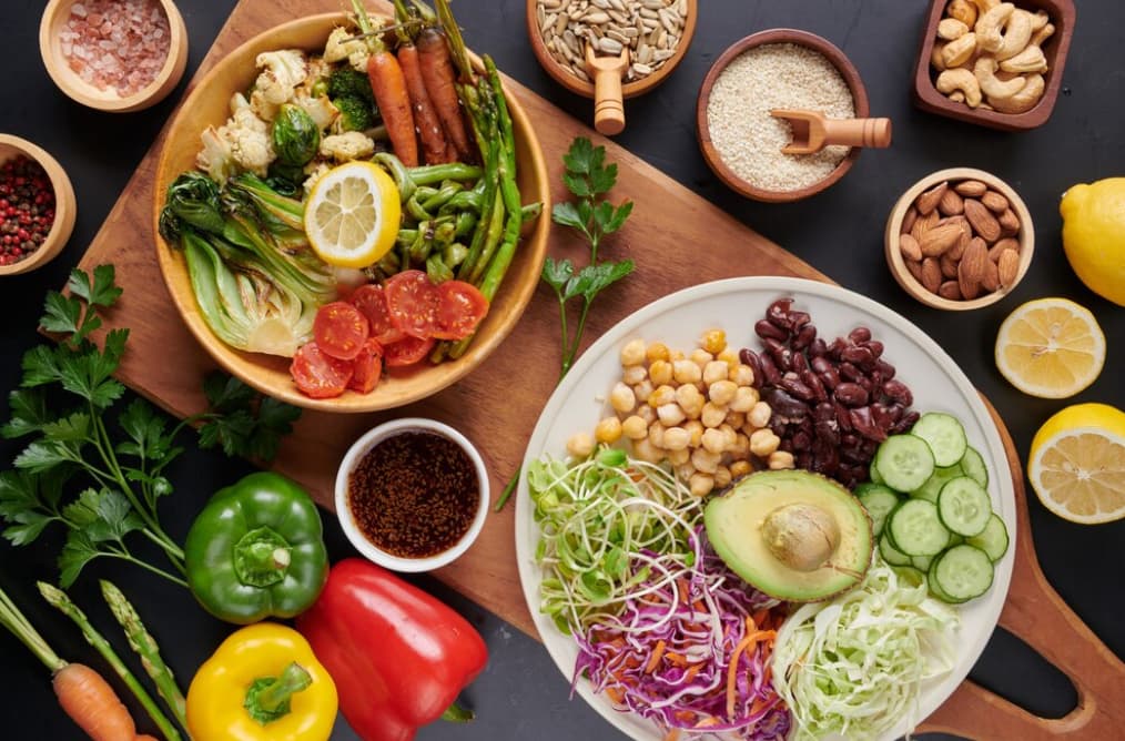 An overhead shot of various fresh vegetables and nuts on a dark surface