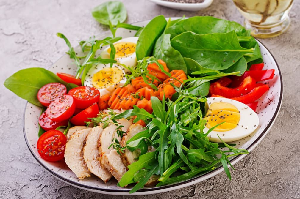 A plate of chicken salad with eggs, tomatoes, and greens on a textured background