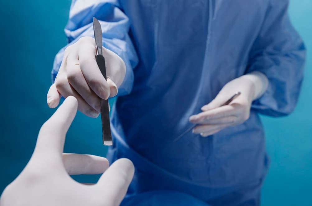 A surgeon's hands holding a scalpel above a simulated patient's hand