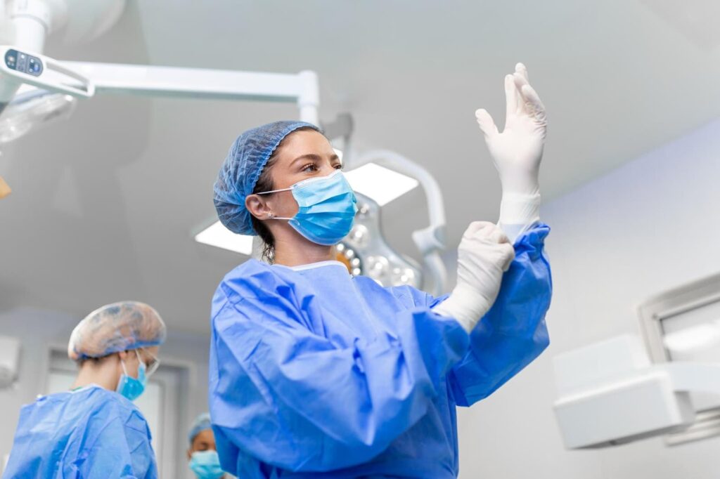 female surgeon putting on medical gloves standing in operating room