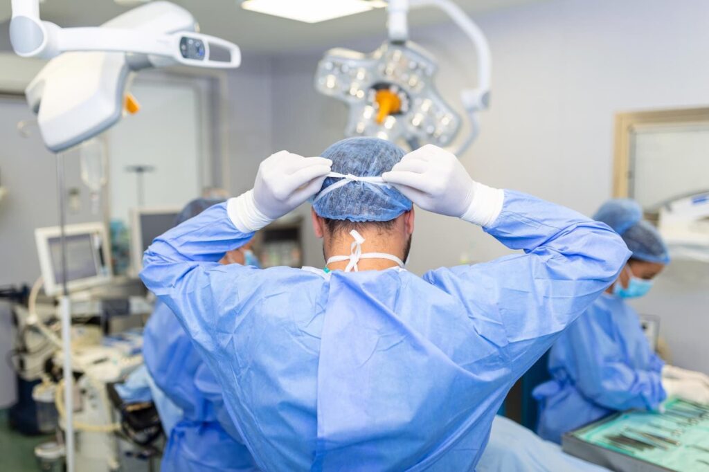 Rear view of male surgeon wearing surgical mask in operation theater at hospital