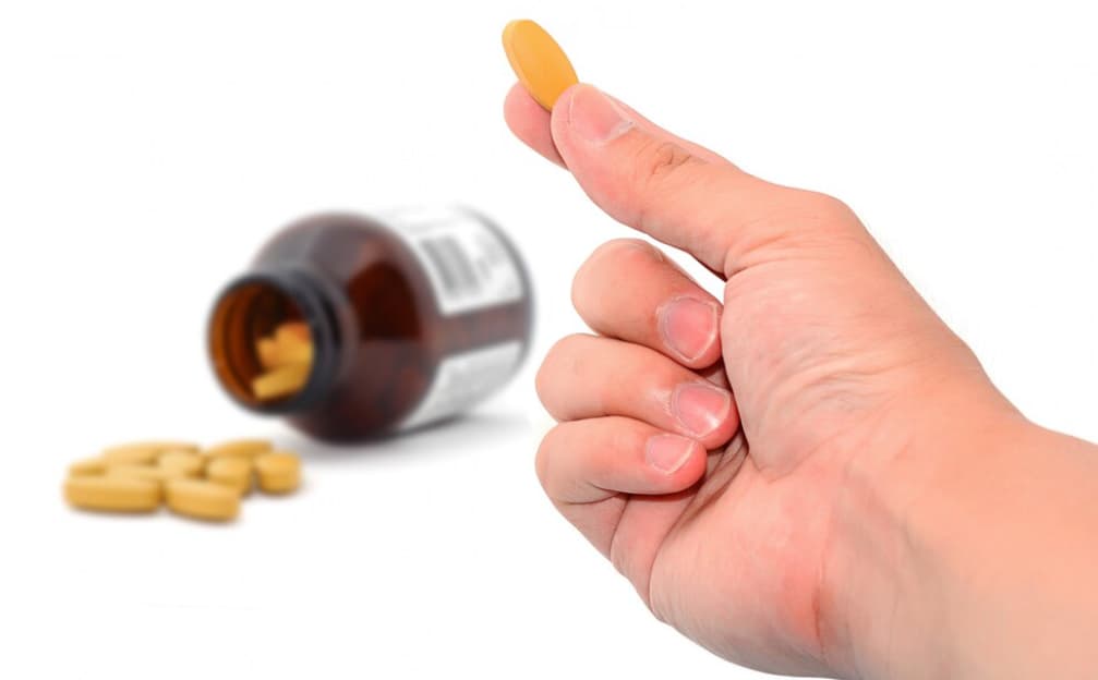 Hand holding a yellow pill with a bottle and pills in the background