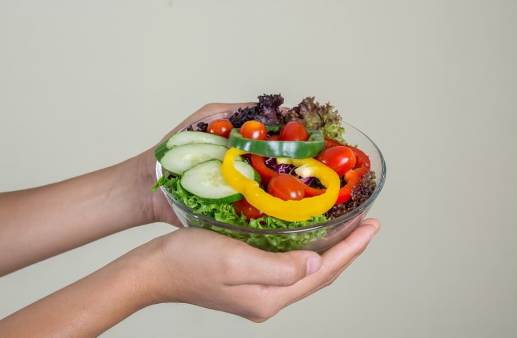 Hands presenting a bowl of fresh mixed salad